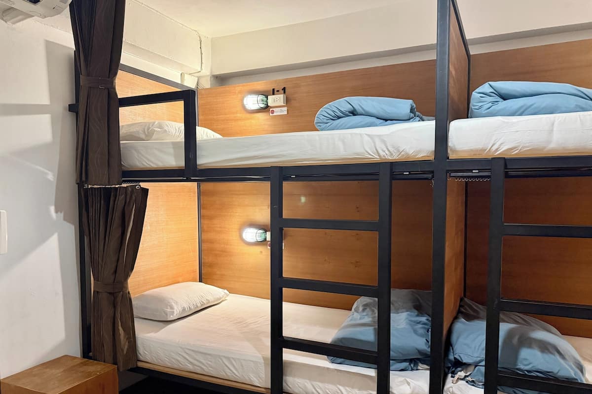 Quarto com beliche, cabeceira de madeira, mesa de cabeceira e luminária na parede.
