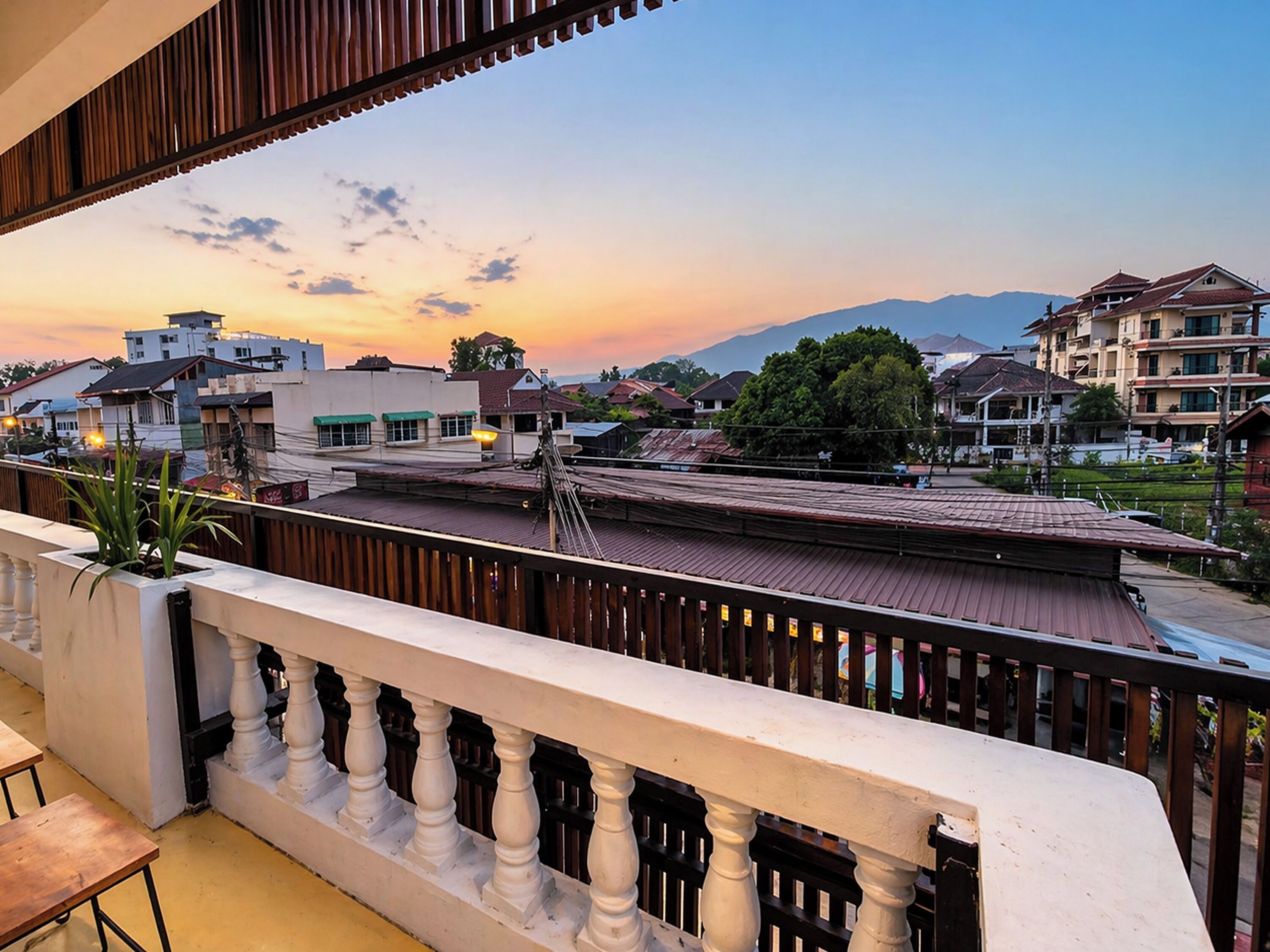 A balcony with a view of a cityscape at sunset, including buildings and mountains.