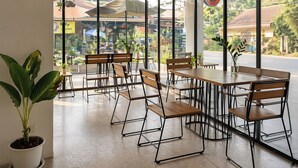 An indoor seating area with tables and chairs, large windows, and potted plants. - Lazy Gibbon 2 Chiang Mai - Haiya (Chiang Mai)