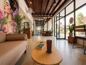 A modern interior with a sofa, a wooden table with a book and a coffee cup, a mural, and large windows. - Lazy Gibbon 2 Chiang Mai - Haiya (Chiang Mai)