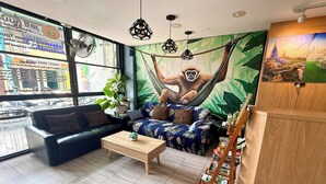 A room with a sofa, a coffee table, a hammock with a monkey, a bookshelf, and a large window with a city view. - Lazy Gibbon 1 Chiang Mai - Tha Phae Gate (Chiang Mai)
