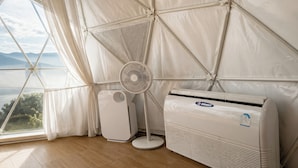 Una habitación con un ventanal grande, un ventilador de pie y un equipo de aire acondicionado.