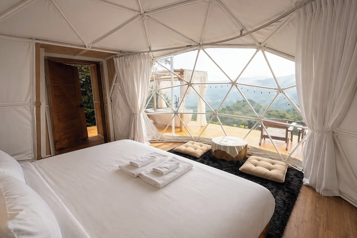 Alojamiento en tienda de campaña con cama, una mesita redonda y vistas del paisaje.