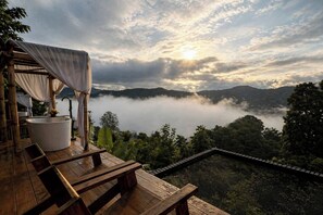Terraza de madera con una bañera blanca y un área de estar cubierta con vistas a un paisaje montañoso.
