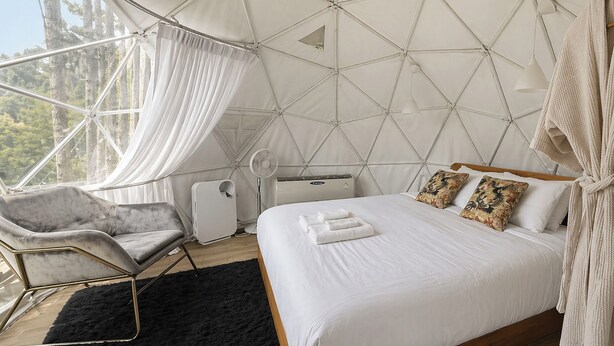 Una habitación con cama, una silla, un ventilador y una ventana con cortinas.
