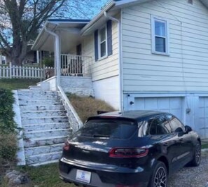 Une voiture noire était garée devant une maison bleu clair, dotée d’un porche et d’un escalier blancs menant à l’entrée.