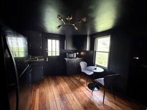 Une cuisine compacte équipée d’un four à micro-ondes, d’une petite table à manger et de deux chaises. Une fenêtre laisse entrer la lumière naturelle et offre une vue sur l’extérieur.