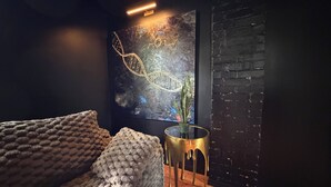 A cozy room with a dark brick wall, a textured sofa, a small round table, and a wall-mounted artwork. - Dark & Cozy Vibez with Appalachian Mountain Views (Candler)