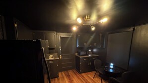 A compact kitchen with wooden flooring, a microwave, a sink, and a small dining area with a chair. - Dark & Cozy Vibez with Appalachian Mountain Views (Candler)