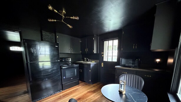 A kitchen with a refrigerator, stove, microwave, and wooden flooring. - Dark & Cozy Vibez with Appalachian Mountain Views (Candler)