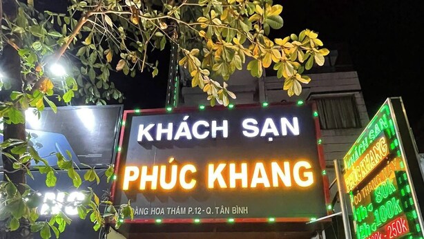 Ein Gebäude mit einem Neonlichtschild mit der Aufschrift 'KHÁCH SAN PHÚC KHANG' und einem Schild mit Preisen.