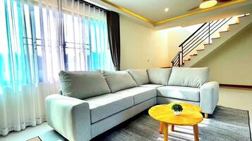 A modern living room with a grey sectional sofa, a small wooden coffee table, and a staircase leading to an upper floor.