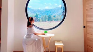 A room with a large round window, a small round table with a plant, and a hanging light fixture. - Chacha Tyme Pool Villa Khaoyai (Pak Chong)