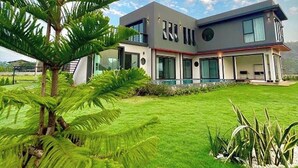 A modern two-story house with a flat roof, large windows, and a well-maintained lawn. - Chacha Tyme Pool Villa Khaoyai (Pak Chong)