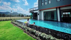 A modern two-story house with a swimming pool, large windows, and a view of the countryside. - Chacha Tyme Pool Villa Khaoyai (Pak Chong)