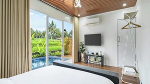Une chambre avec un lit, une télévision, un portant à vêtements et une vue sur une piscine et un espace verdoyant.