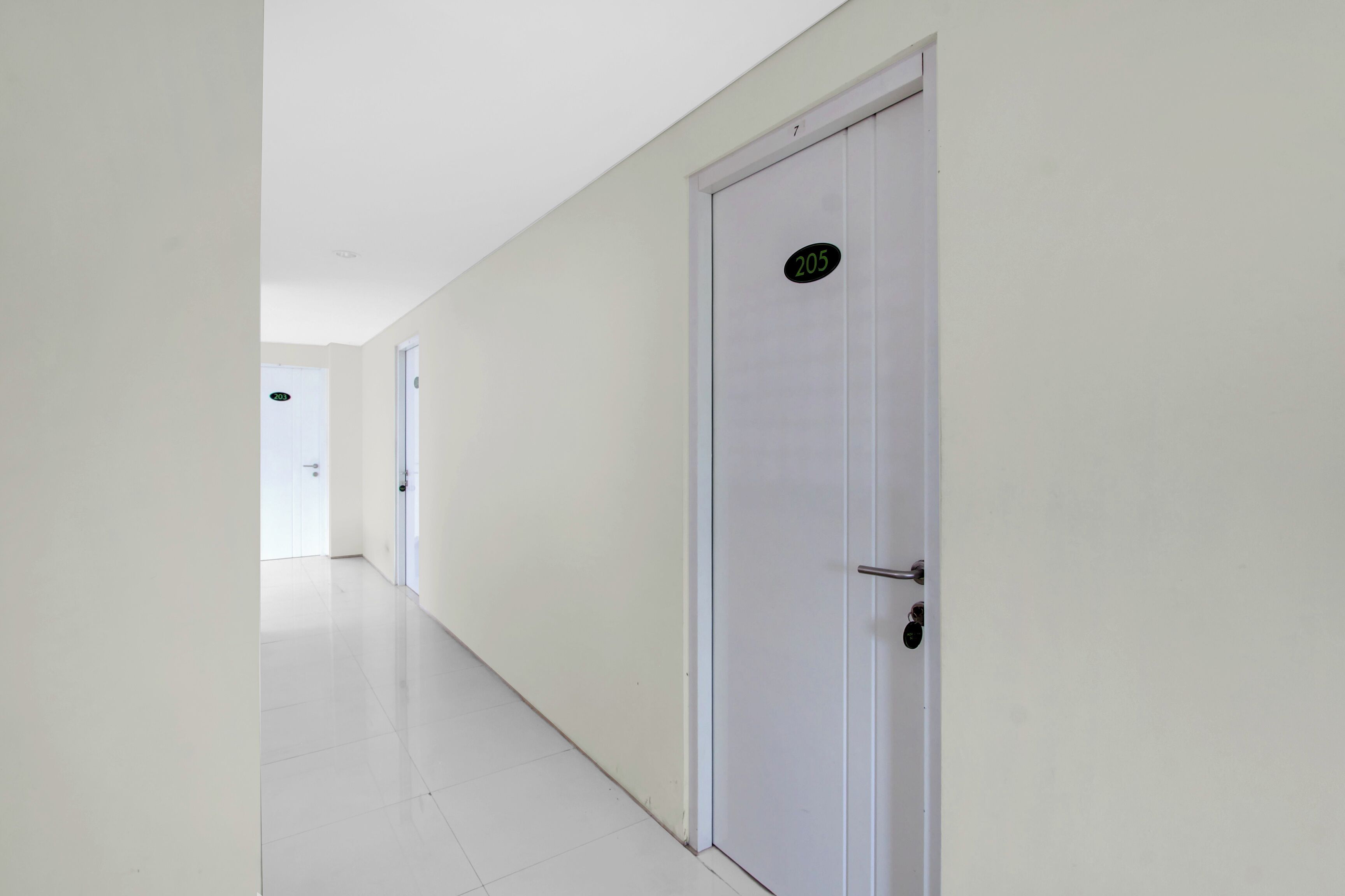 Un pasillo con paredes y puertas blancas, una de ellas con el número 205.
