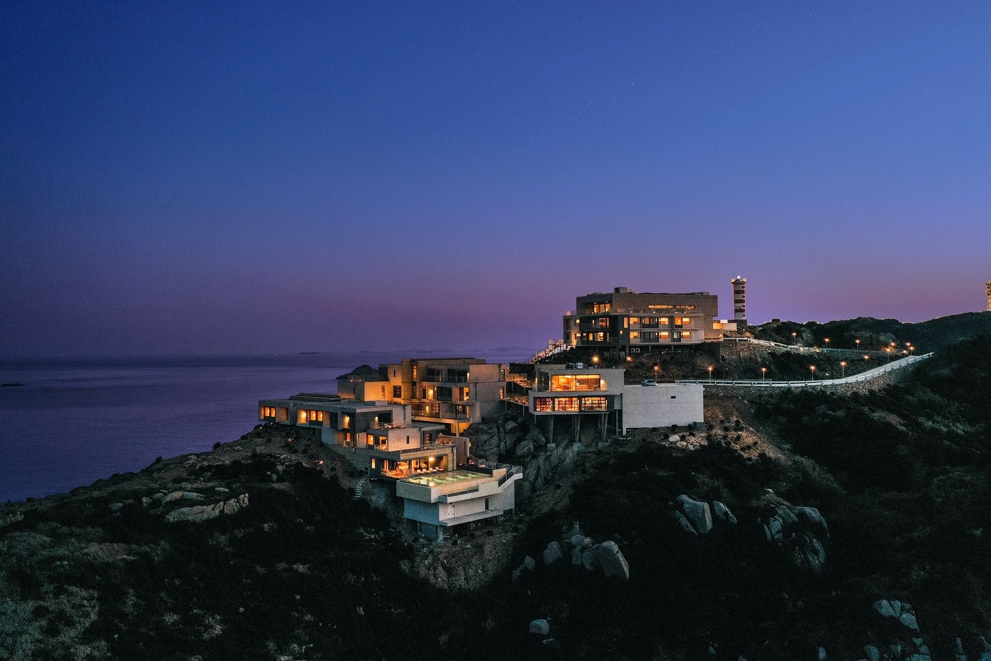 A coastal property with multiple buildings, a lighthouse, and a paved pathway.