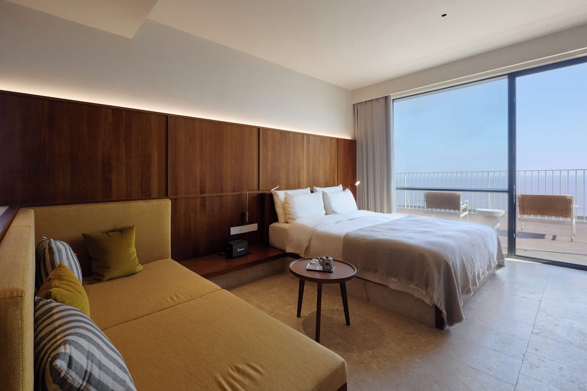 Habitación de hotel con cama, sofá, una mesita y balcón con vistas.