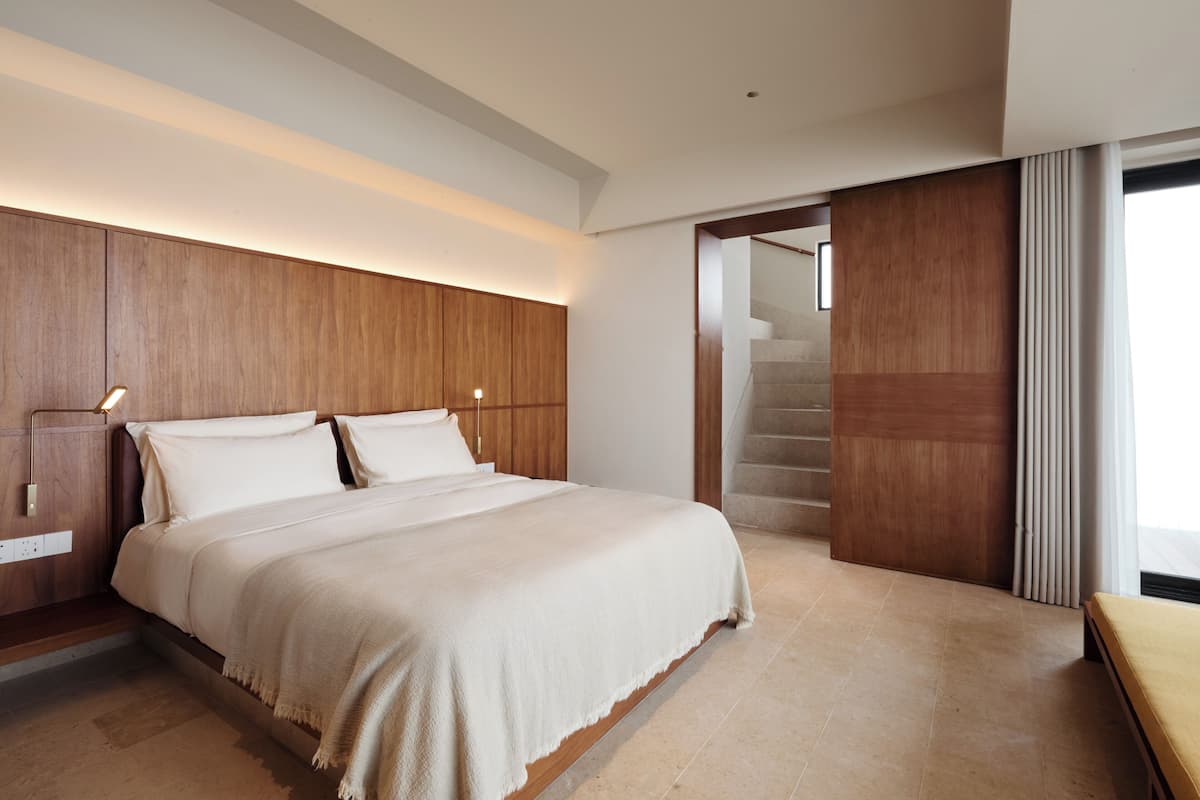 Un dormitorio moderno con una cama grande, cabecera de madera y una escalera que conduce a un nivel superior.