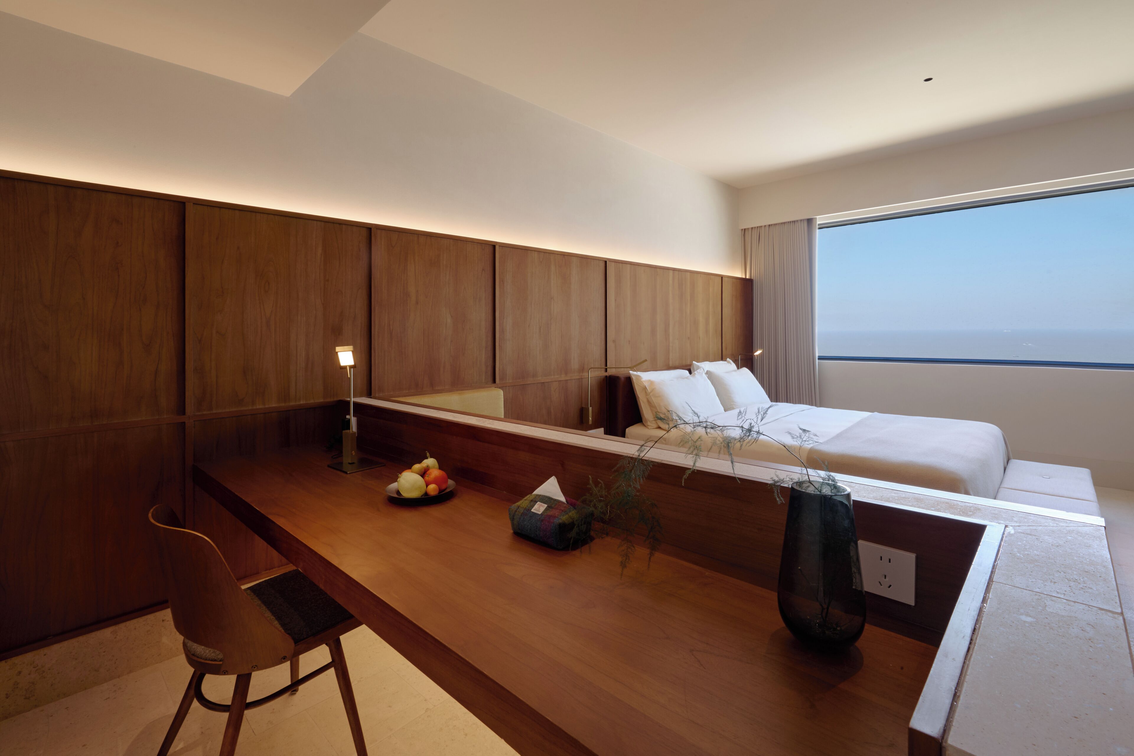 Habitació d'hotel moderna amb escriptori de fusta, un llit i una finestra gran.