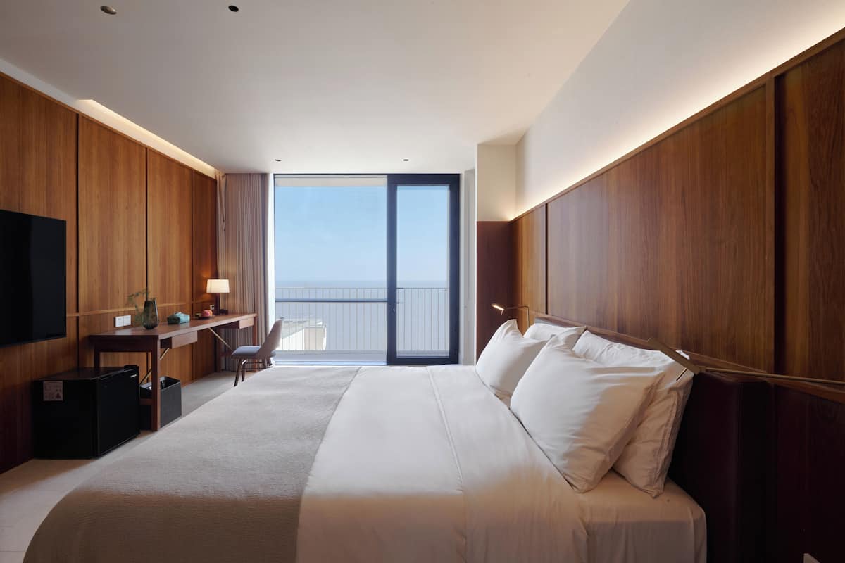 Habitación de hotel con una cama grande, un escritorio, una silla, un televisor y un balcón con vistas.