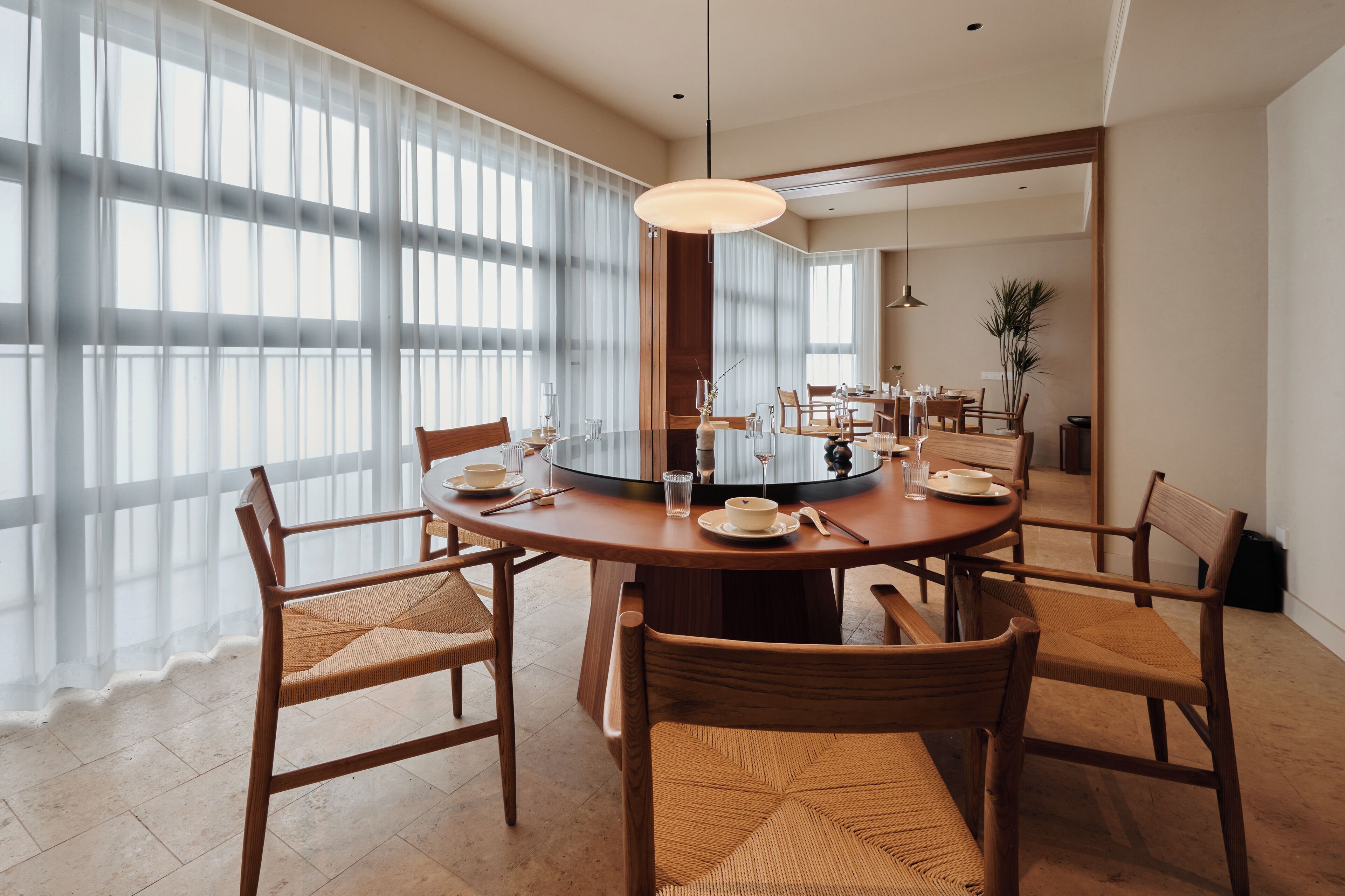 Een moderne eetruimte met een ronde tafel, houten stoelen en een groot raam met lichte gordijnen.