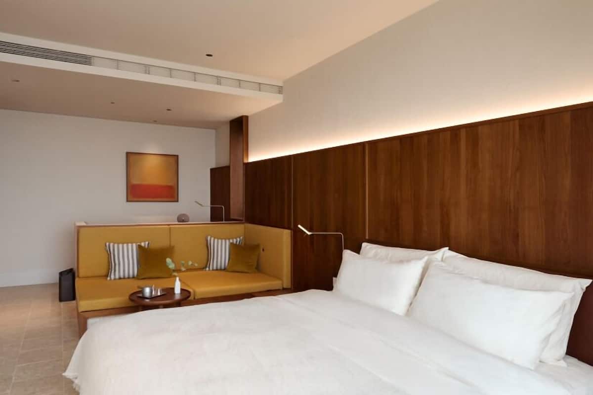 Una habitación de hotel con una cama grande, un sofá, una mesita y una obra de arte colgada en la pared.