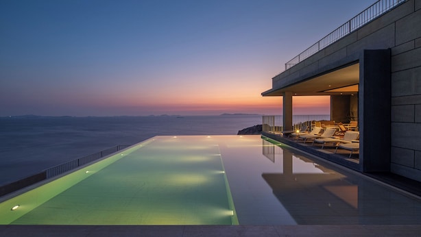A modern infinity pool with a clear view of the ocean at sunset.