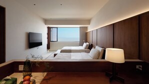 A hotel room with a bed, a TV, a window with a view, a lamp, and a vase with plants.