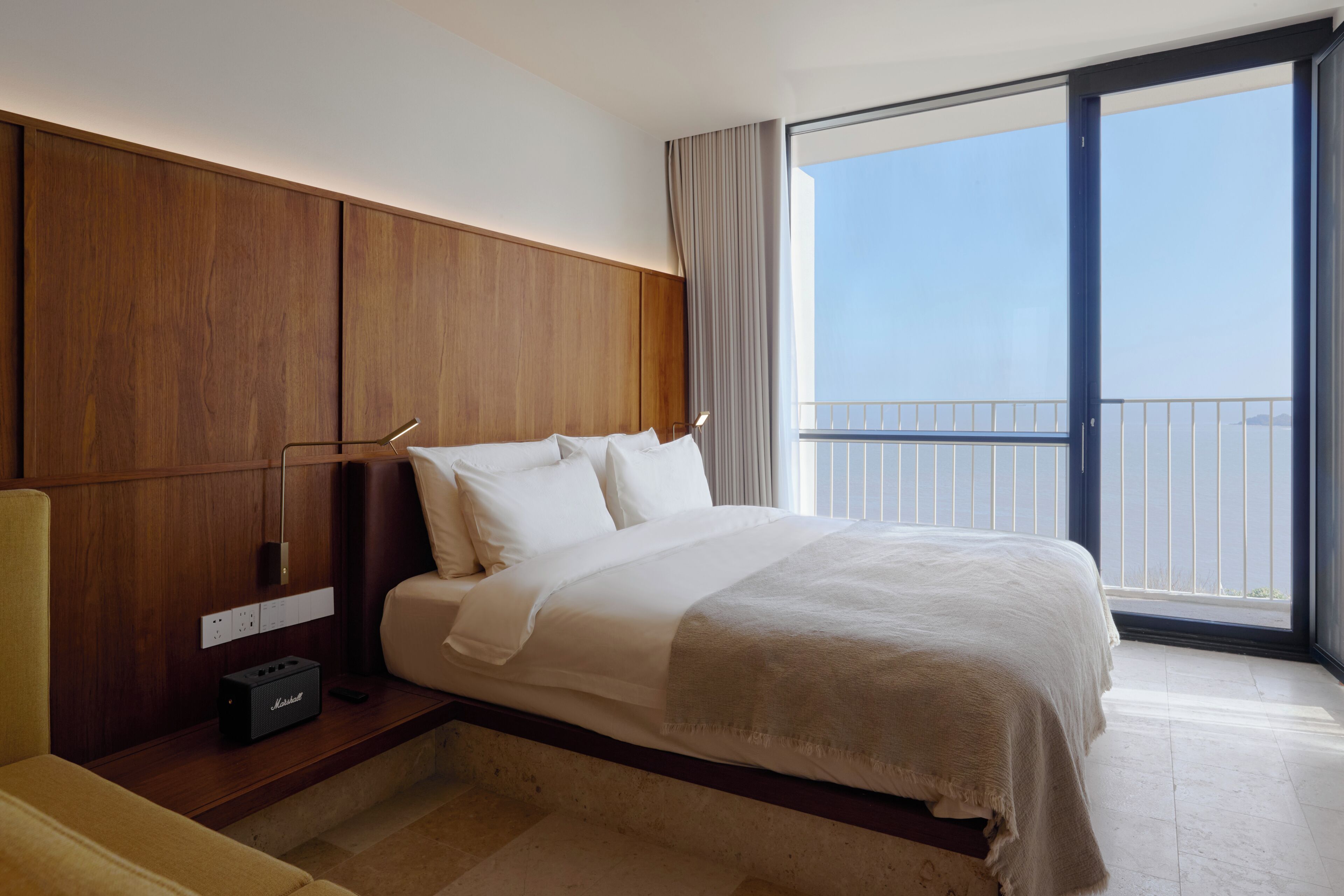 A modern hotel room with a large bed, wooden paneling, a view of the balcony, and a flat-screen TV.