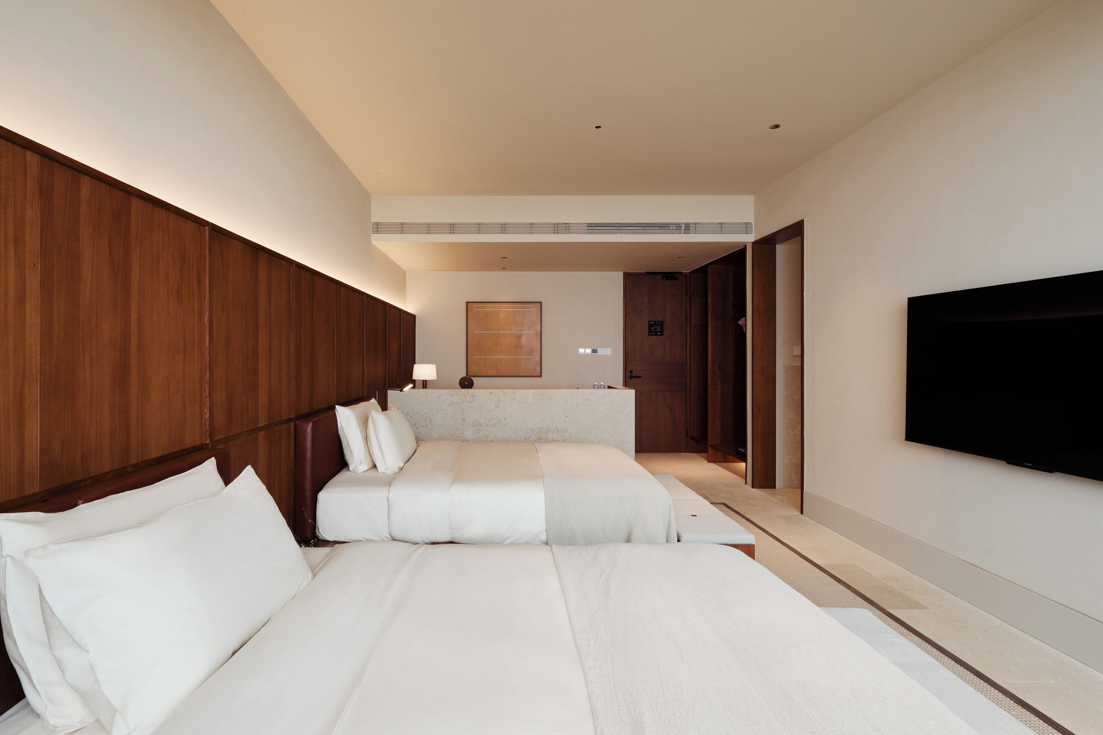 A hotel room with a large bed, a TV mounted on the wall, and a wooden headboard.