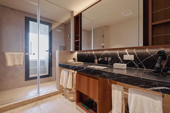 Une salle de bain moderne avec un grand miroir, un comptoir en marbre noir, un espace douche et un meuble-lavabo en bois.