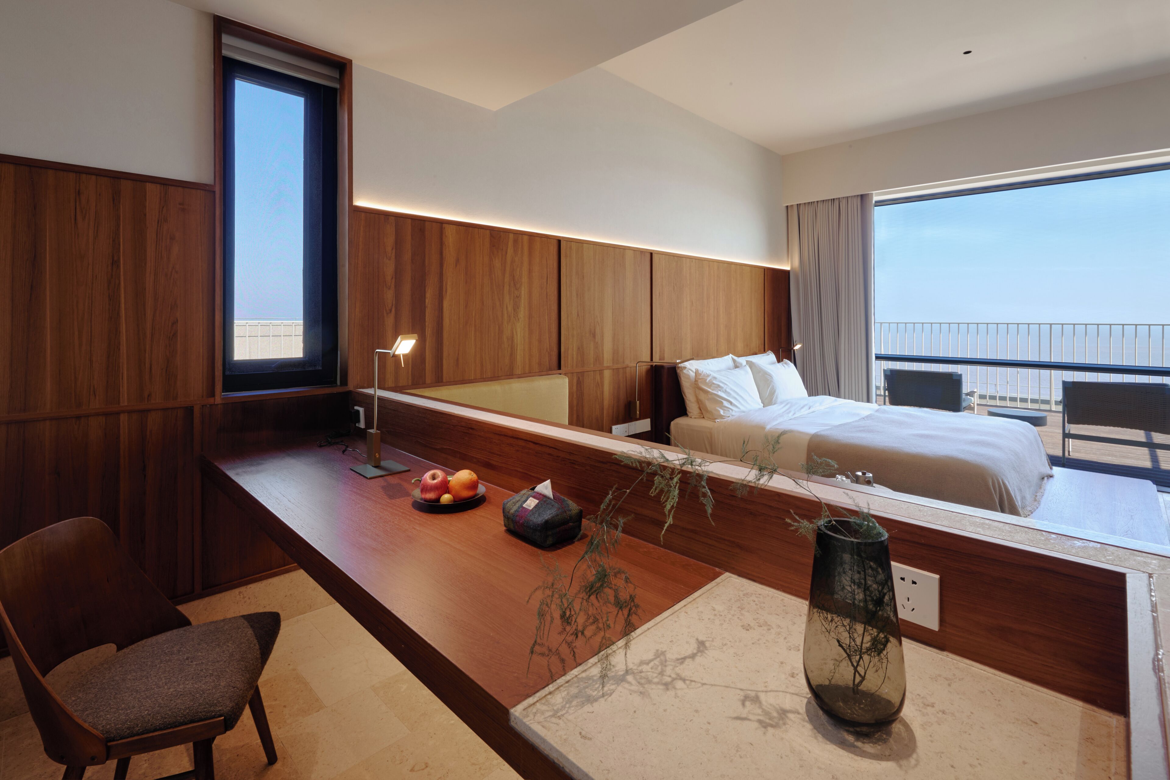 Et moderne hotelværelse med et træskrivebord, en stol, en seng og et stort vindue.