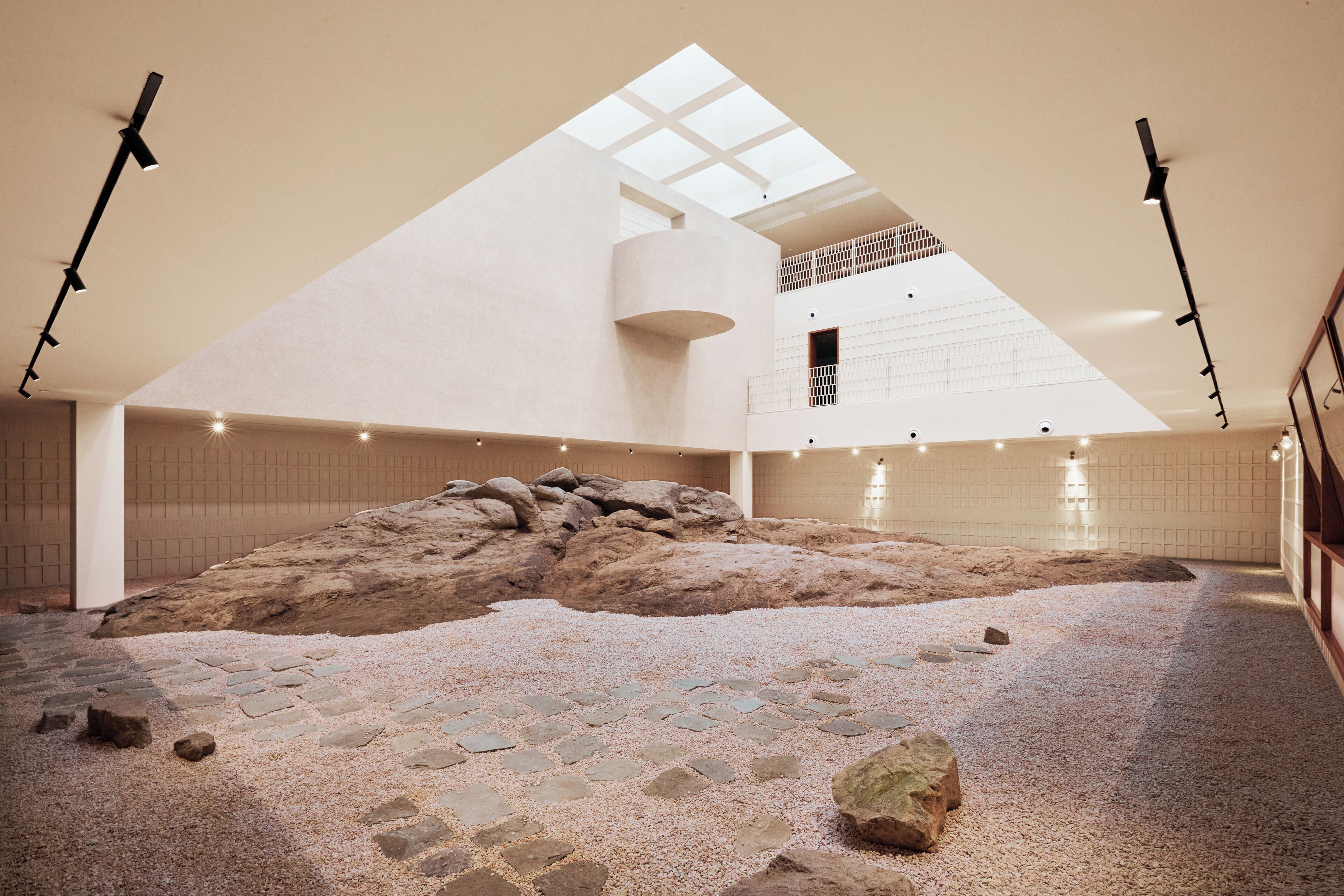 A spacious interior with a high ceiling, a central rock formation, and a skylight.