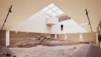 A spacious interior with a high ceiling, a central rock formation, and a skylight.