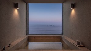 A bathtub with a view of the sea, a towel, and a small container.