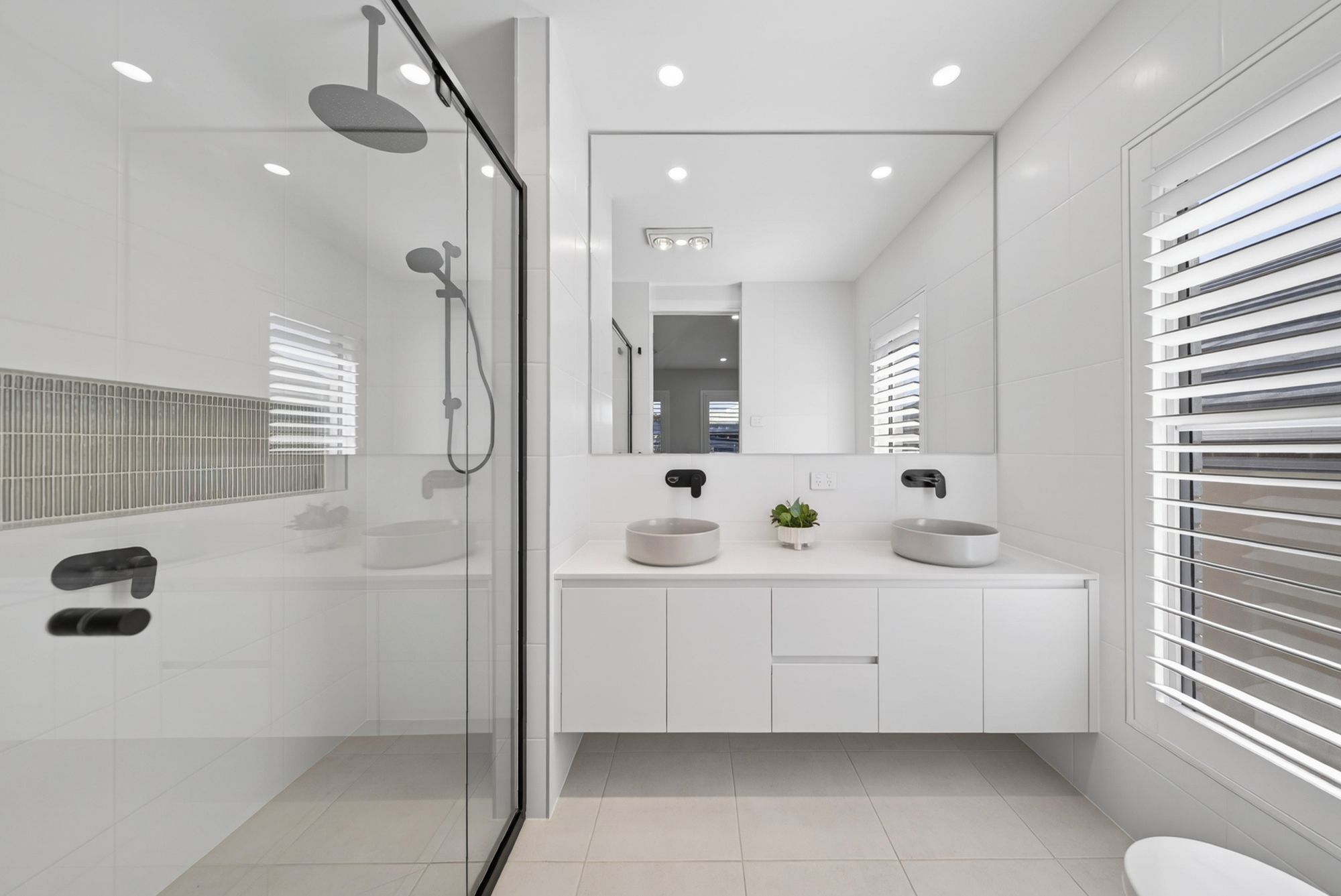 A modern bathroom with a glass shower enclosure, two sinks, a mirror, and a toilet.