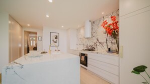 A modern kitchen with a marble countertop, white cabinetry, a built-in oven, and a marble backsplash.