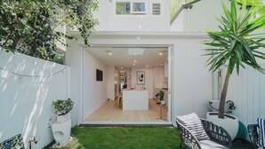 A modern house with a small backyard, a dining area, and a kitchen visible through an open door.