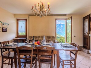 Un coin repas agrémenté d’un lustre, de chaises en bois, d’une table dressée pour quatre personnes et offrant une vue sur les montagnes grâce à de grandes fenêtres.