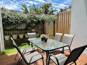 A patio with a glass table and chairs, surrounded by potted plants and a wooden fence. - Designer 4-Bed Coastal Home Walk To Beach & Shops (Maroubra)