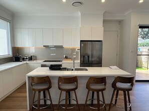 Eine moderne Küche mit weißen Schränken, einem Edelstahl-Kühlschrank, einem Einbauofen und einer Bar mit Hockern.