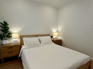 A bedroom with a bed, two bedside tables, a nightstand, a potted plant, and a lamp. - Designer 4-Bed Coastal Home Walk To Beach & Shops (Maroubra)