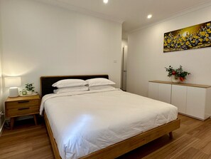Ein Schlafzimmer mit einem hölzernen Bett, einem Nachttisch, einer Nachttischlampe, einem an der Wand befestigten Regal mit einer Vase und einem Gemälde.