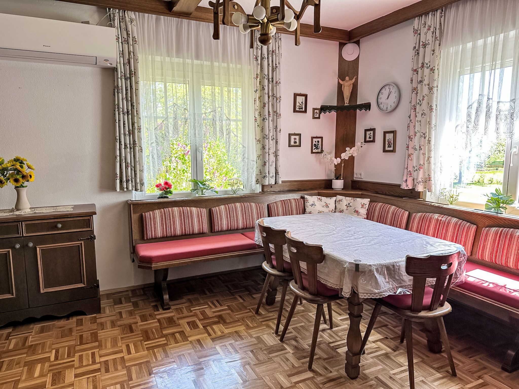 Un espace repas doté d’un parquet en bois disposé en motif chevron, d’une table ronde recouverte d’une nappe blanche et d’un banc agrémenté de coussins à rayures.