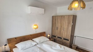 A bedroom with a wooden bed, white linens, a wardrobe, a wall-mounted heater, and a ceiling light fixture. - Haus Kühnsdorf by Interhome (Klopeiner See)
