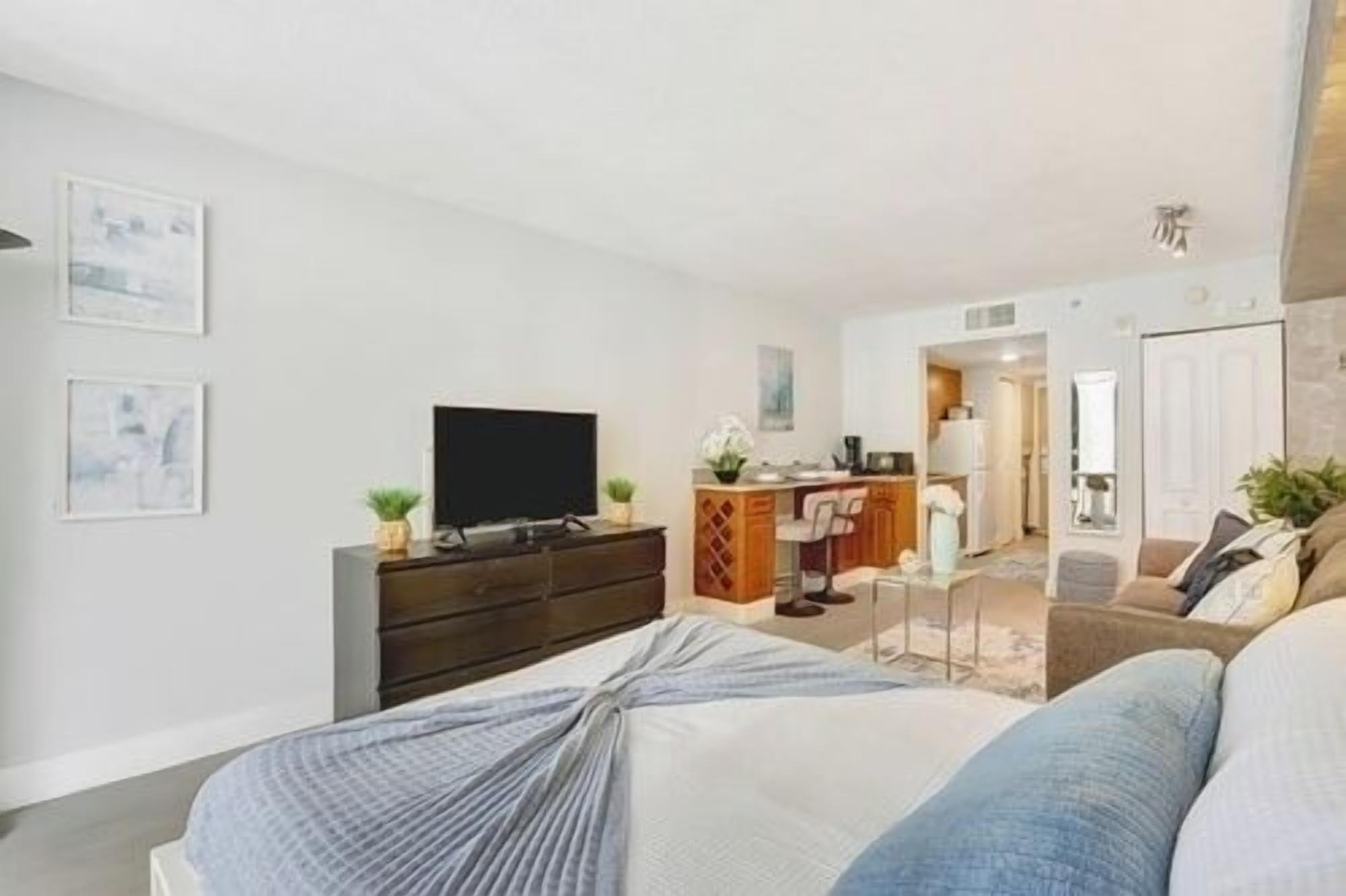 A modern bedroom with a bed, a TV, a dresser, and a desk area.