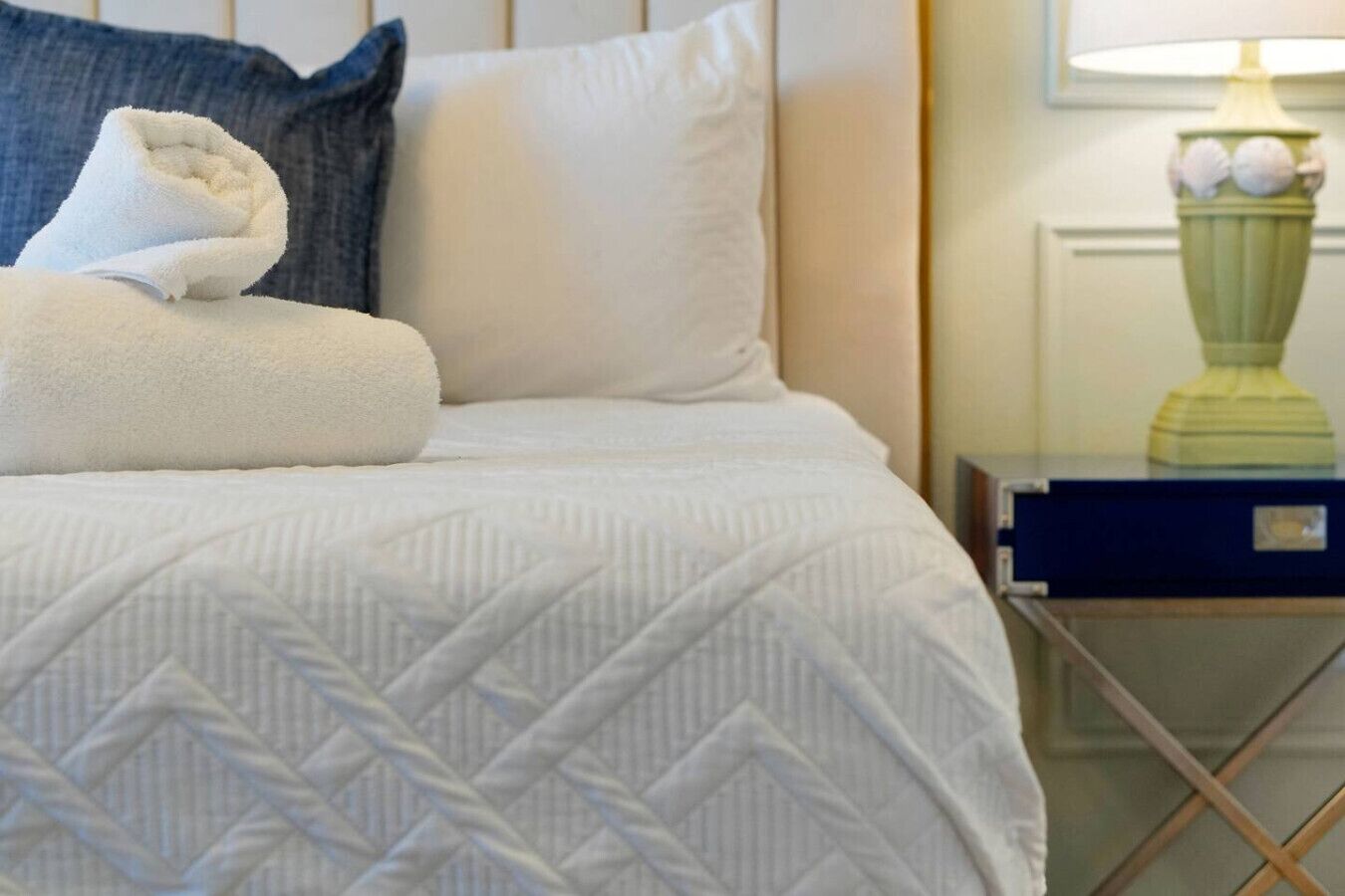 Un lit bien fait, avec une couette blanche, une serviette pliée et un oreiller.