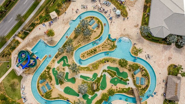 An aerial view of a resort with a winding pool, lounge areas, and a water slide.